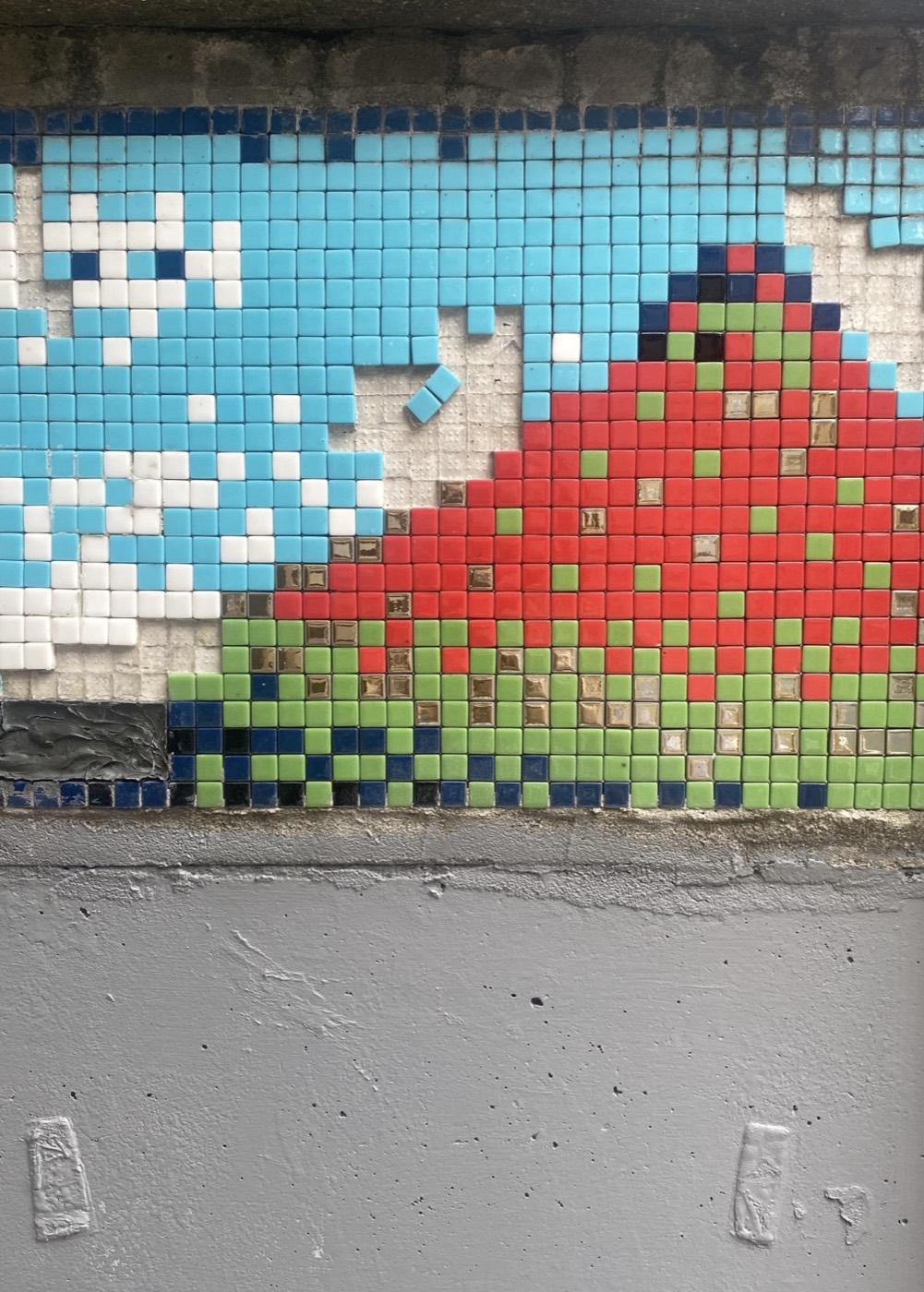 Photograph of a tiled wall mosaic with a red and green mountain under pixel clouds