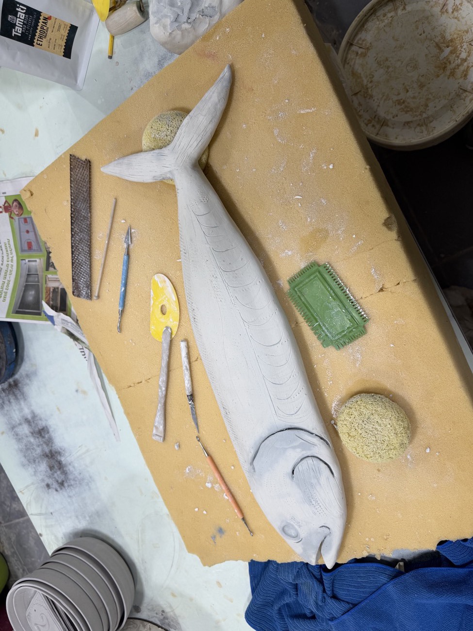 Unfired clay fish sculpture on a workbench with tools